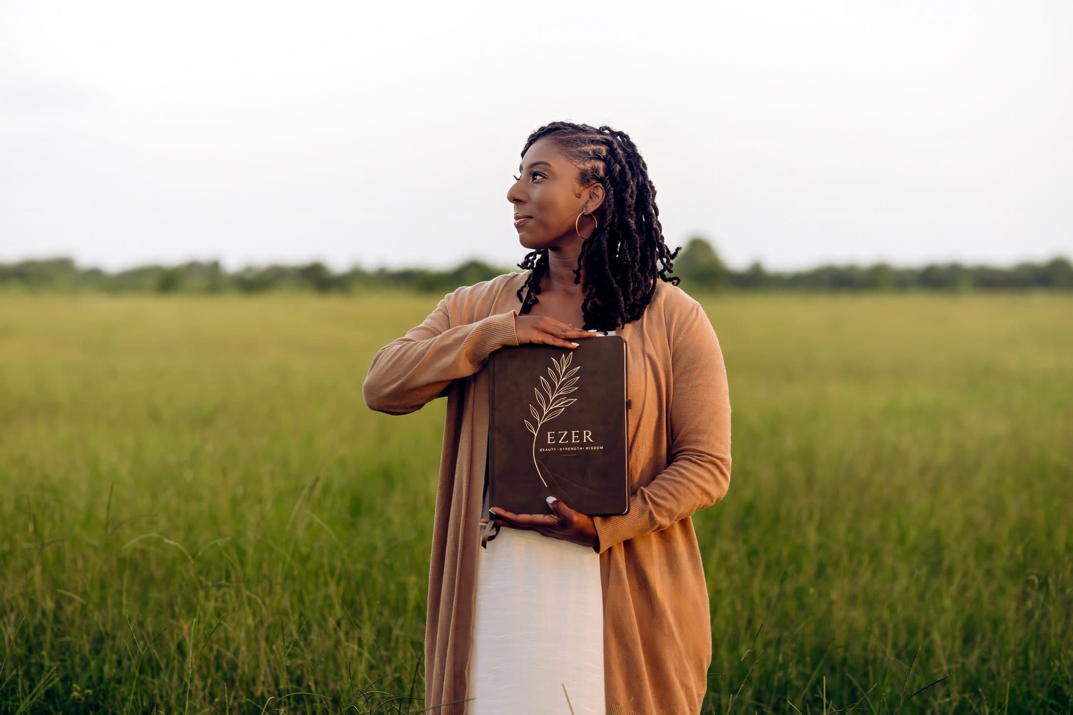 A woman holding the Ezer Planner while standing in a golden field